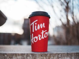 Red Tim Horton coffee cup placed on a concrete surface with a blurred outdoor background.