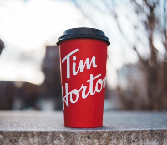 Red Tim Horton coffee cup placed on a concrete surface with a blurred outdoor background.