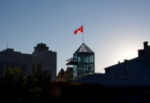 Playteck: 20 лет создания легкоатлетических дорожек в Канаде Silhouette of Winnipeg skyline with Canadian flag during sunset, showcasing modern architecture.