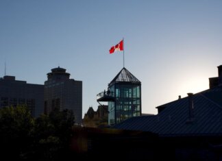 Playteck: 20 лет создания легкоатлетических дорожек в Канаде Silhouette of Winnipeg skyline with Canadian flag during sunset, showcasing modern architecture.