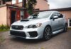 Subaru стала партнёром чемпионата по триатлону в Виктории Silver Subaru WRX STI parked in a residential driveway with rustic backdrop.