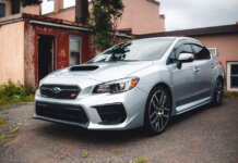 Silver Subaru WRX STI parked in a residential driveway with rustic backdrop.