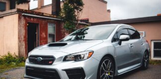 Silver Subaru WRX STI parked in a residential driveway with rustic backdrop.