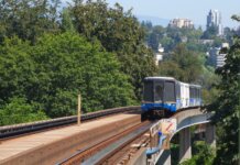 SkyTrain travels on elevated tracks through New Westminster, surrounded by lush greenery.