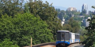 SkyTrain travels on elevated tracks through New Westminster, surrounded by lush greenery.