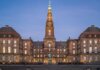Stunning evening view of Christiansborg Palace with its illuminated spire in Copenhagen, Denmark.