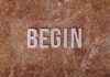 Text 'BEGIN' on a textured stone background, symbolizing a fresh start.