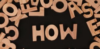 Top view of scattered wooden letters with 'HOW' centered on a dark surface, promoting inquiry.