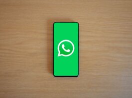 Top view of smartphone displaying WhatsApp logo on a wooden background, representing technology and communication.