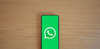 Top view of smartphone displaying WhatsApp logo on a wooden background, representing technology and communication.