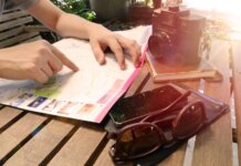 Планируете летние поездки? CBSA даёт советы по въезду в Канаду Traveler pointing at map on wooden table with camera and accessories under sunlight.