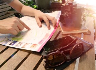 Traveler pointing at map on wooden table with camera and accessories under sunlight.