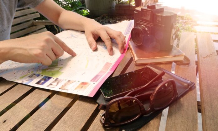 Traveler pointing at map on wooden table with camera and accessories under sunlight. Traveler pointing at map on wooden table with camera and accessories under sunlight.