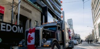Truck convoy with Canadian flag during protest in downtown street. Demonstration for freedom movement.