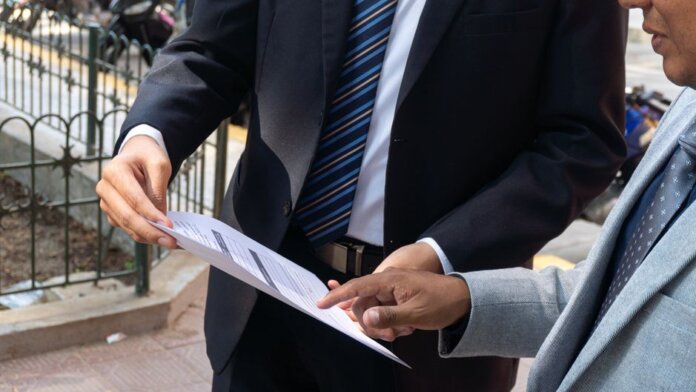Two business professionals discussing and exchanging documents outdoors in Piura, Peru. Two business professionals discussing and exchanging documents outdoors in Piura, Peru.