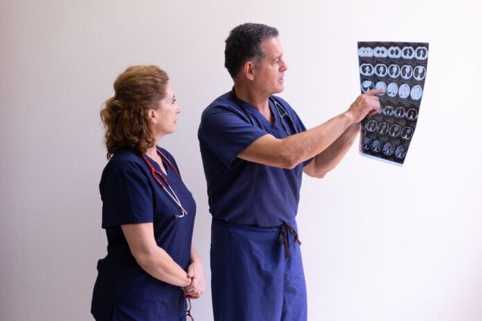 Two healthcare professionals in scrubs examining a medical x-ray image, discussing diagnosis. Two healthcare professionals in scrubs examining a medical x-ray image, discussing diagnosis.