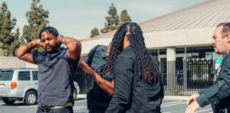 Two law enforcement officers detain a man during a daytime arrest outside a building.