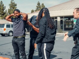Two law enforcement officers detain a man during a daytime arrest outside a building.