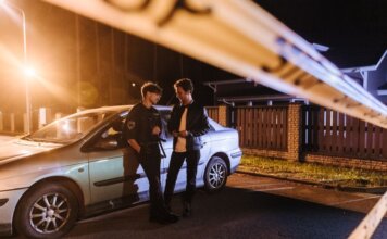 Полиция разыскивает двух мужчин за мошенничество с банковскими картами Two men discussing at a nighttime urban crime scene with police tape and a car.