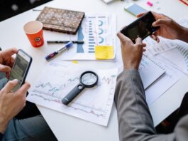 Two professionals analyzing data and graphs with smartphones on a white table.