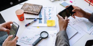 Two professionals analyzing data and graphs with smartphones on a white table.