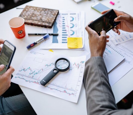 Two professionals analyzing data and graphs with smartphones on a white table.