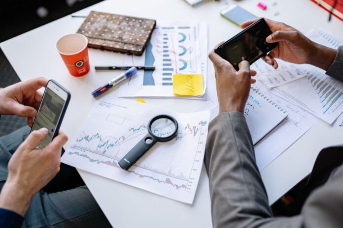 Two professionals analyzing data and graphs with smartphones on a white table. Two professionals analyzing data and graphs with smartphones on a white table.