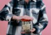 Консерваторы требуют от Карни представить план по снятию пошлин США Woman in plaid shirt holds money jar with travel goals in mind.