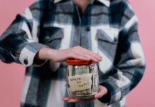 Консерваторы требуют от Карни представить план по снятию пошлин США Woman in plaid shirt holds money jar with travel goals in mind.
