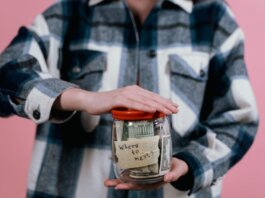 Woman in plaid shirt holds money jar with travel goals in mind.