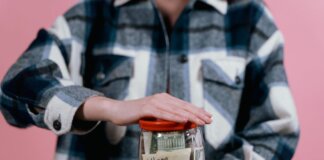 Woman in plaid shirt holds money jar with travel goals in mind.