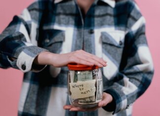 Консерваторы требуют от Карни представить план по снятию пошлин США Woman in plaid shirt holds money jar with travel goals in mind.