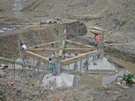 Workers constructing a building foundation with rebar and wooden supports outdoors.