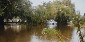 A car struggles through a flooded street surrounded by trees after a heavy rainstorm.