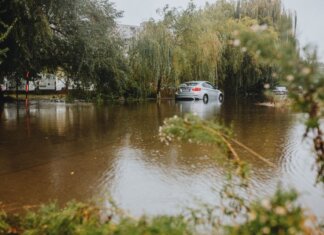 A car struggles through a flooded street surrounded by trees after a heavy rainstorm.