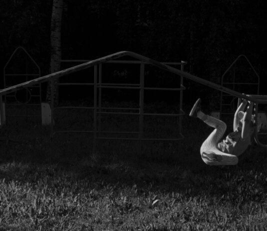 A child gracefully swings on monkey bars at a playground, captured in a black and white image.