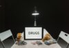 A dimly lit room with a sign displaying 'DRUGS' surrounded by money and illegal substances.