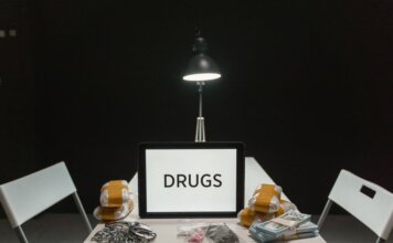 Полиция Реджайны изъяла крупную партию фентанила после двухмесячного расследования A dimly lit room with a sign displaying 'DRUGS' surrounded by money and illegal substances.