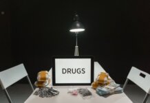 В Лондоне изъяты винтовка и кокаин на $25 тысяч A dimly lit room with a sign displaying 'DRUGS' surrounded by money and illegal substances.