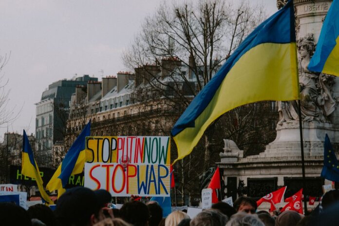 A dynamic crowd in Paris rallies with Ukrainian flags and anti-war signs, advocating peace. A dynamic crowd in Paris rallies with Ukrainian flags and anti-war signs, advocating peace.