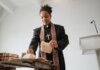 A female priest breaking bread at the altar during a religious service indoors, symbolizing unity and faith.