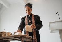 A female priest breaking bread at the altar during a religious service indoors, symbolizing unity and faith.