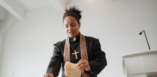 A female priest breaking bread at the altar during a religious service indoors, symbolizing unity and faith.