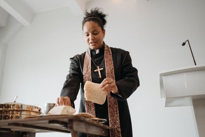 A female priest breaking bread at the altar during a religious service indoors, symbolizing unity and faith. A female priest breaking bread at the altar during a religious service indoors, symbolizing unity and faith.
