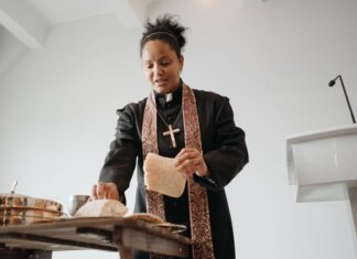 A female priest breaking bread at the altar during a religious service indoors, symbolizing unity and faith.