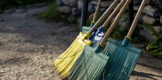 A group of colorful brooms standing on a dirt path outdoors, perfect for cleaning themes.