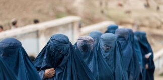 A group of women covered in blue burqas walking outdoors in Afghanistan, highlighting cultural attire.