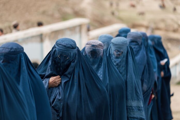 A group of women covered in blue burqas walking outdoors in Afghanistan, highlighting cultural attire. A group of women covered in blue burqas walking outdoors in Afghanistan, highlighting cultural attire.
