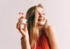 A happy woman in red holding a cupcake with a Canadian flag toothpick against a white background.