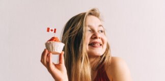 A happy woman in red holding a cupcake with a Canadian flag toothpick against a white background.
